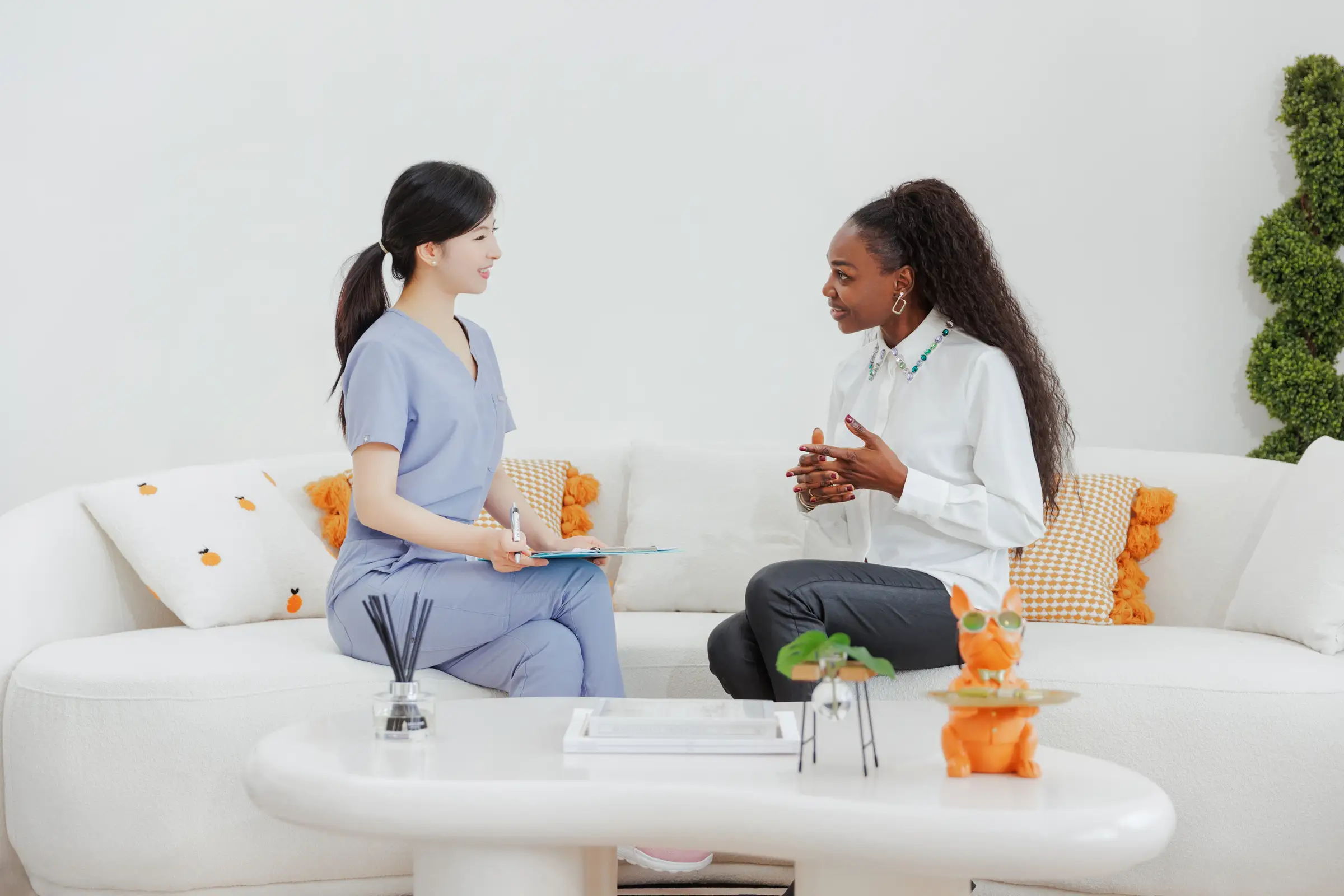 Su Dou, RPN, listening to a client on the sofa at S.D. Medical Spa, clipboard and pen in hand.
