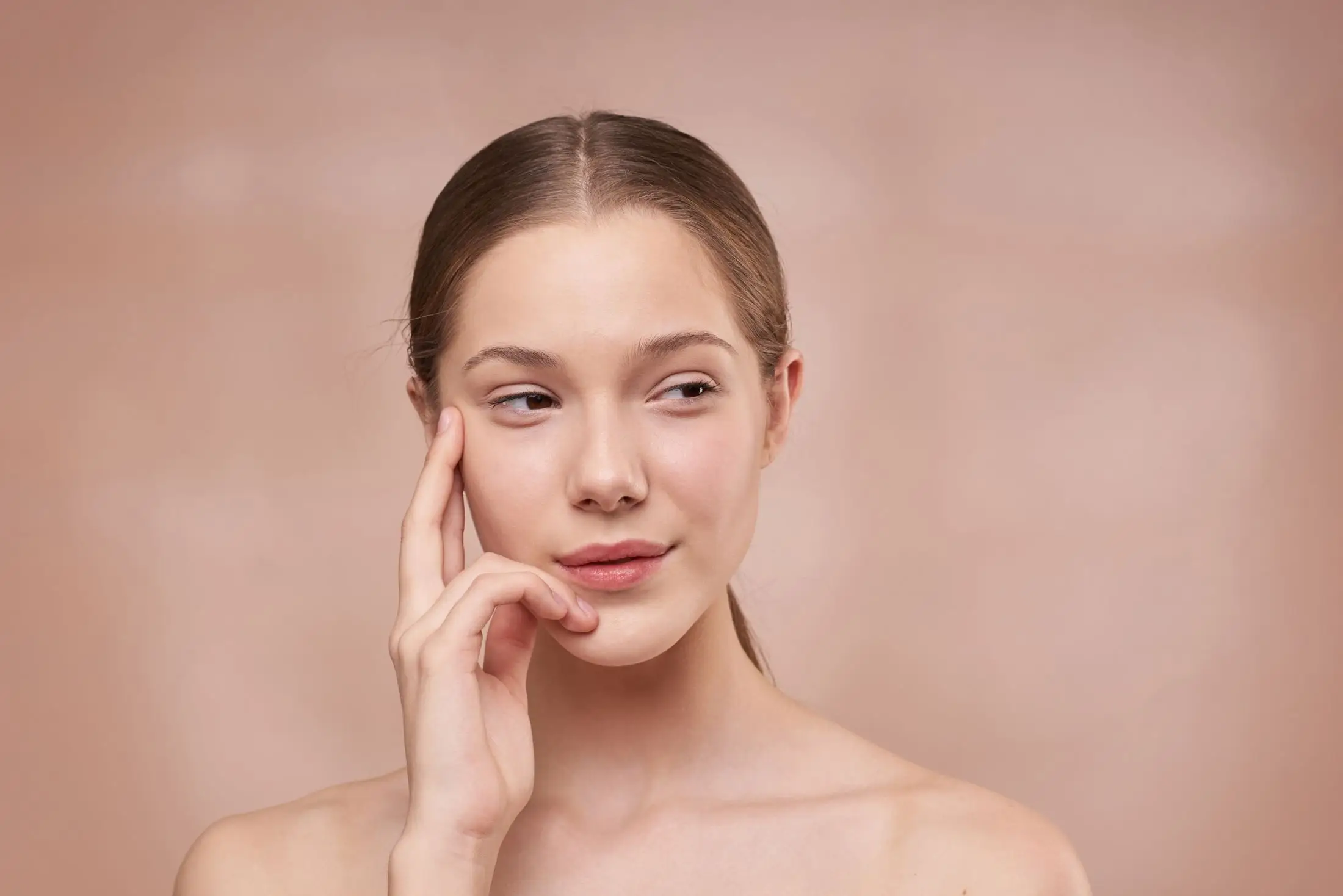 A woman touching her cheekbone with her fingertips.