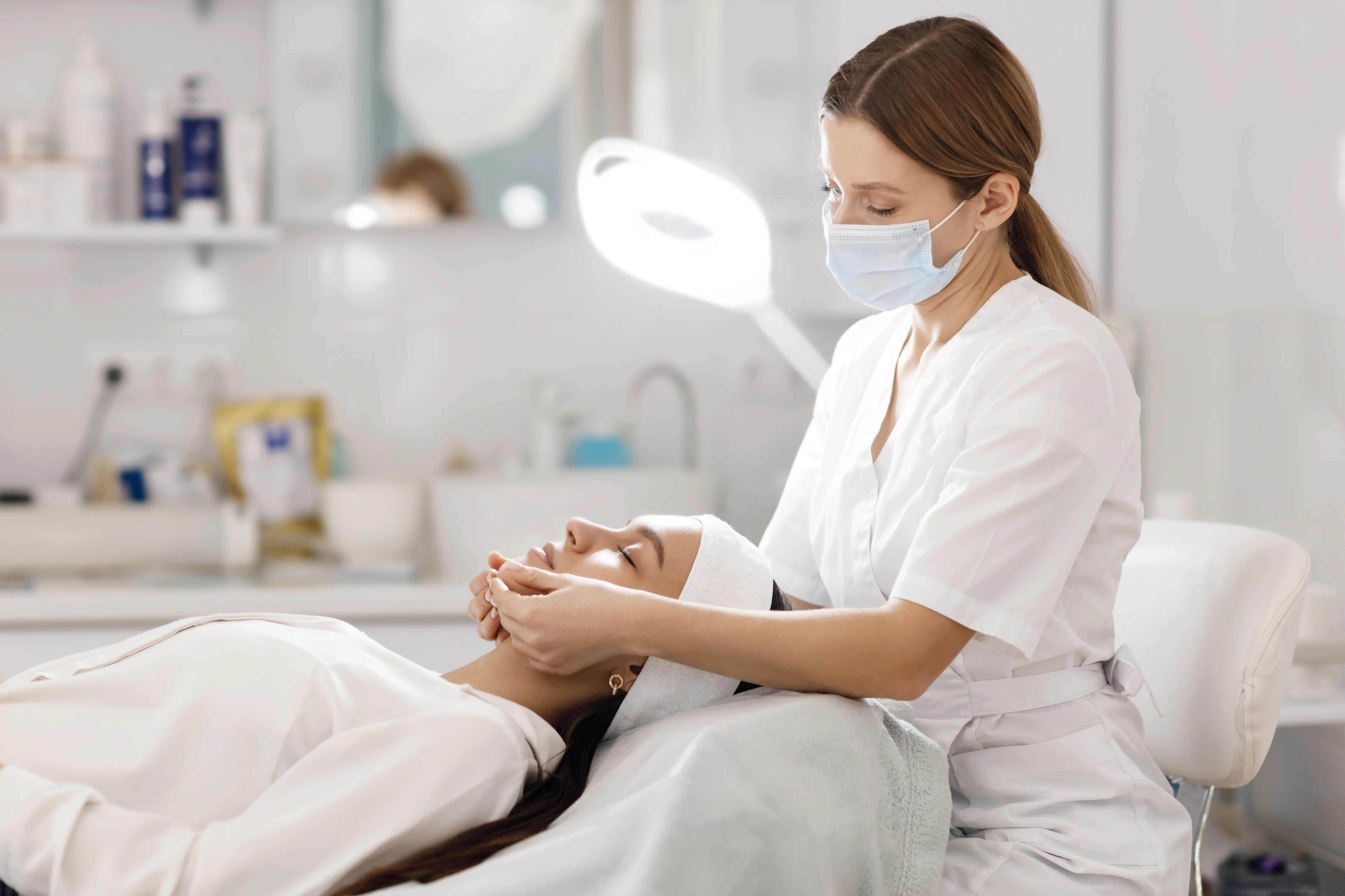 A masked practitioner holding a reclining client’s jaw in both hands in a treatment room.