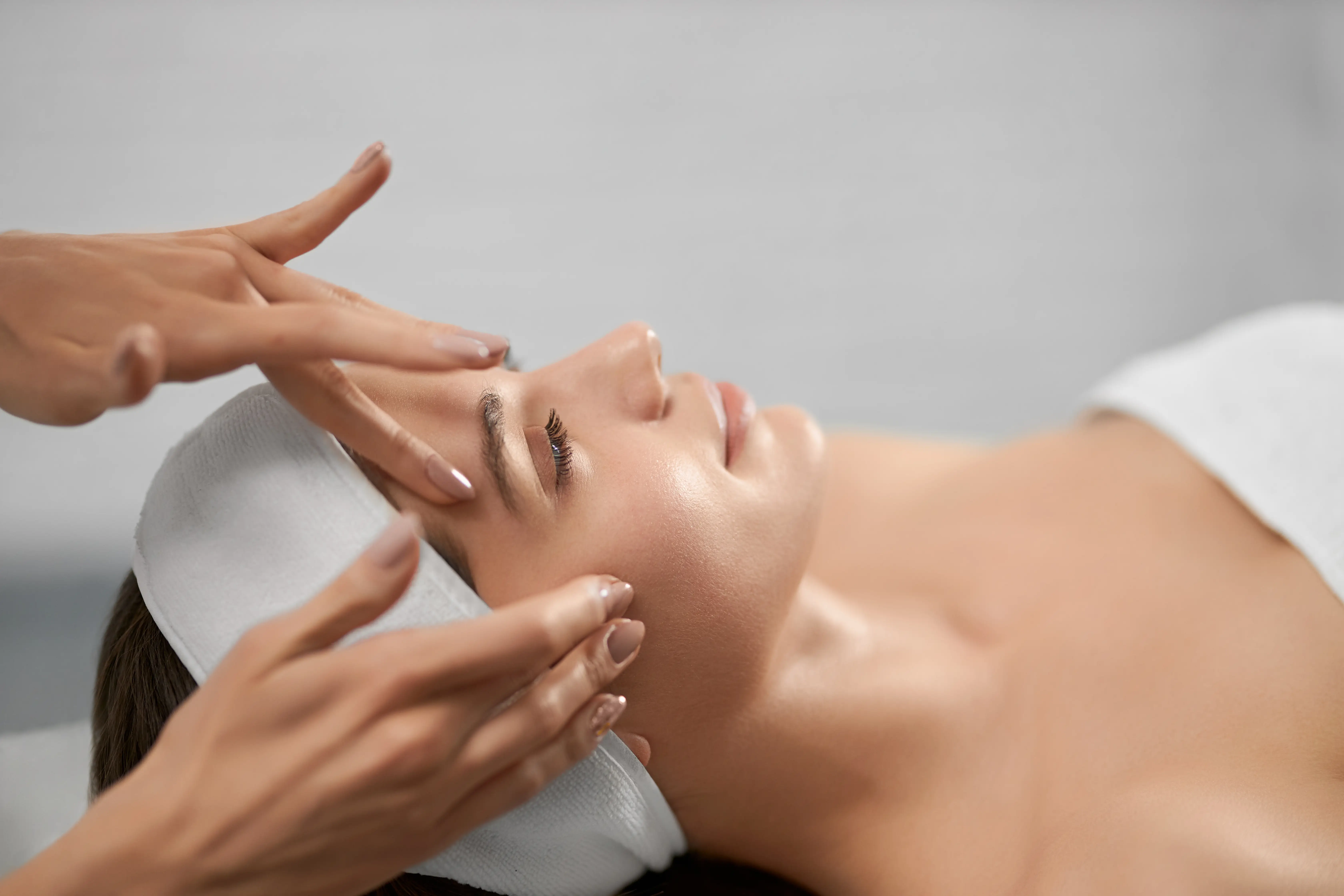 Hands performing a facial massage on a client lying on a treatment bed.
