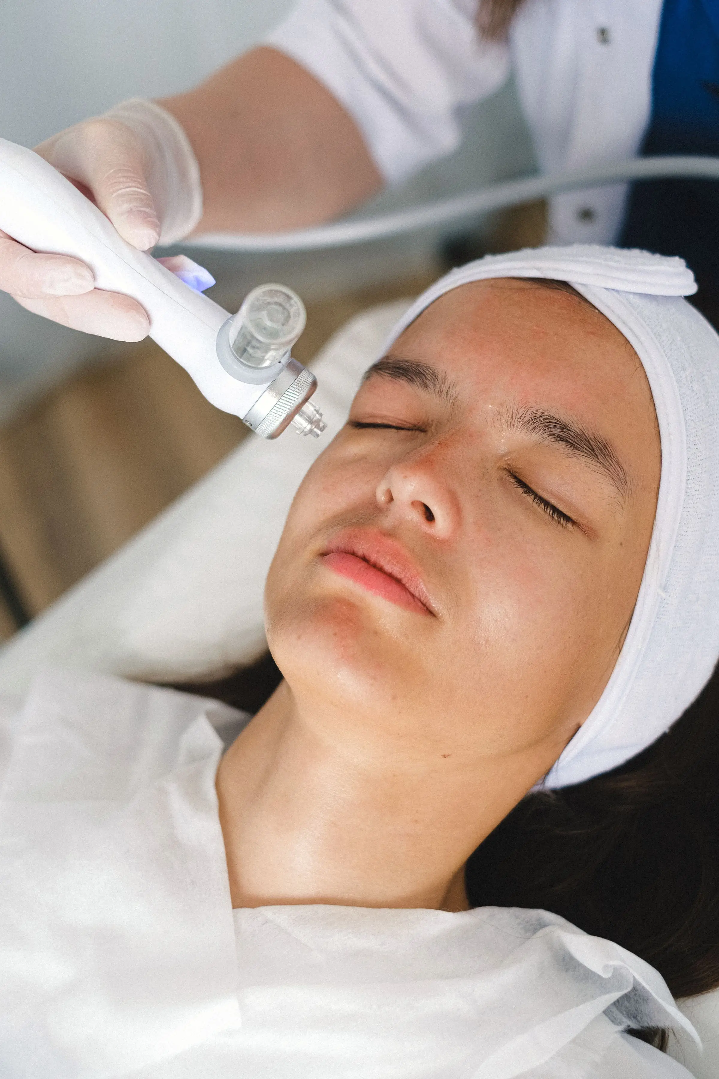 A gloved hand holding a treatment probe against a client’s cheek.